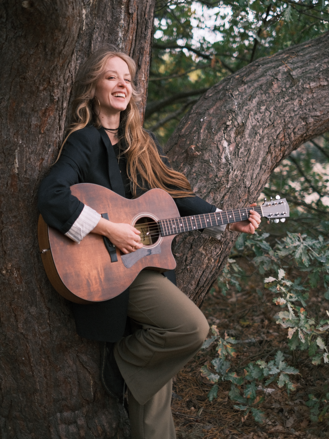 Zangeres Rachelle Adriënne speelt leunend tegen een boom gitaar in Breda